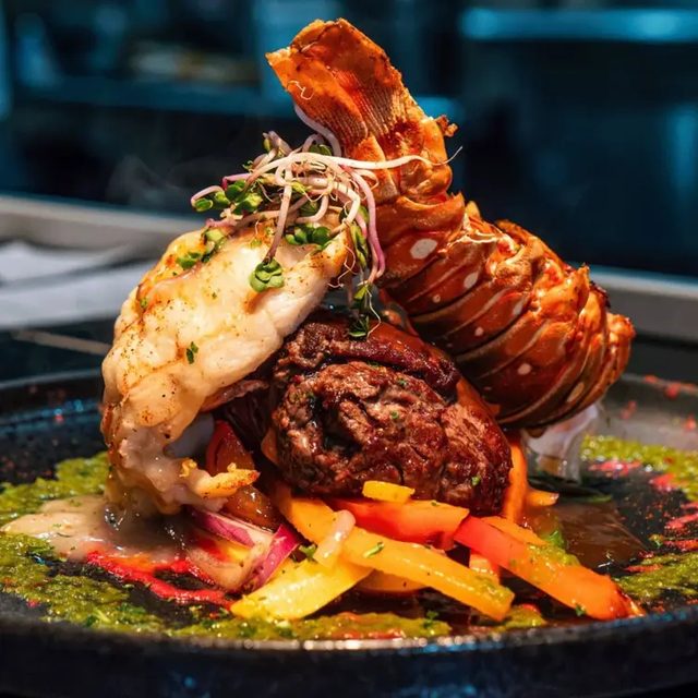 Surf and turf — una cola de langosta y carne de res en un plato oscuro con pimientos