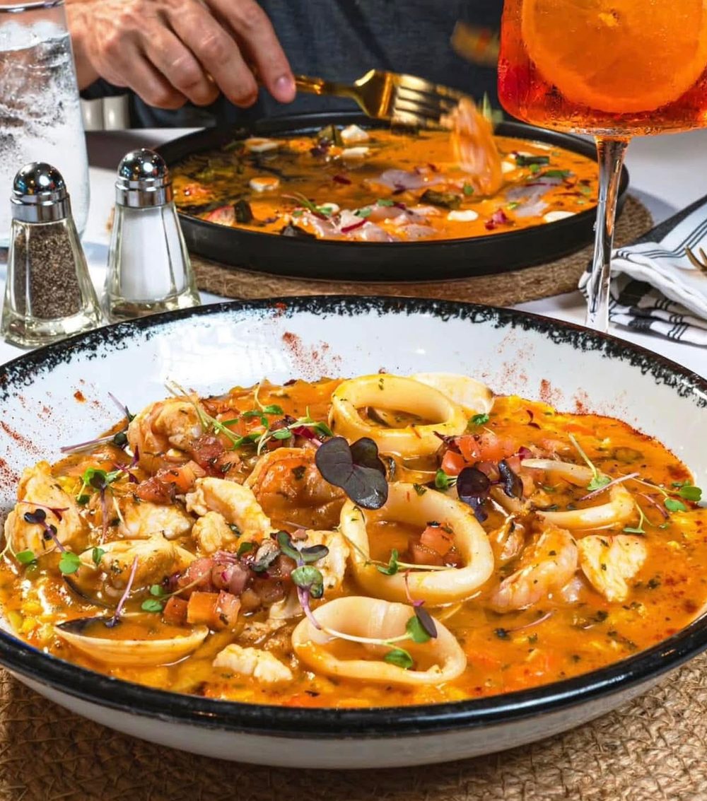 A seafood bowl of fish, calamari and shrimp in saffron broth, laid for two