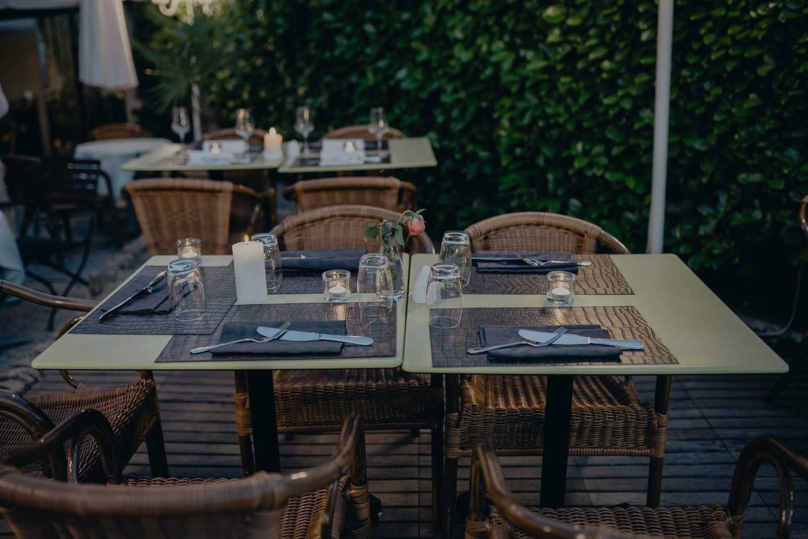 A terrace table laid for dinner at dusk — folded napkins, glasses, a lit pillar candle and a single rose