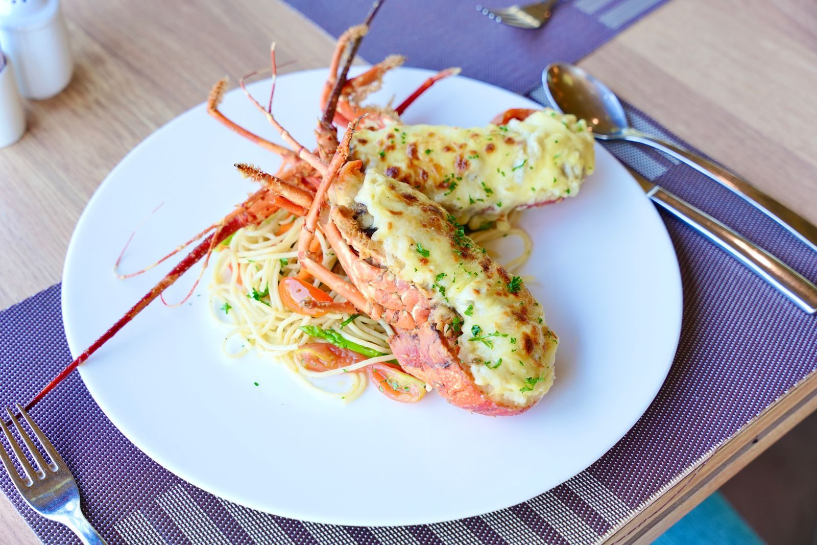 A lobster split lengthways, both half-shells filled with a browned cheese and cream gratin, served over thin pasta