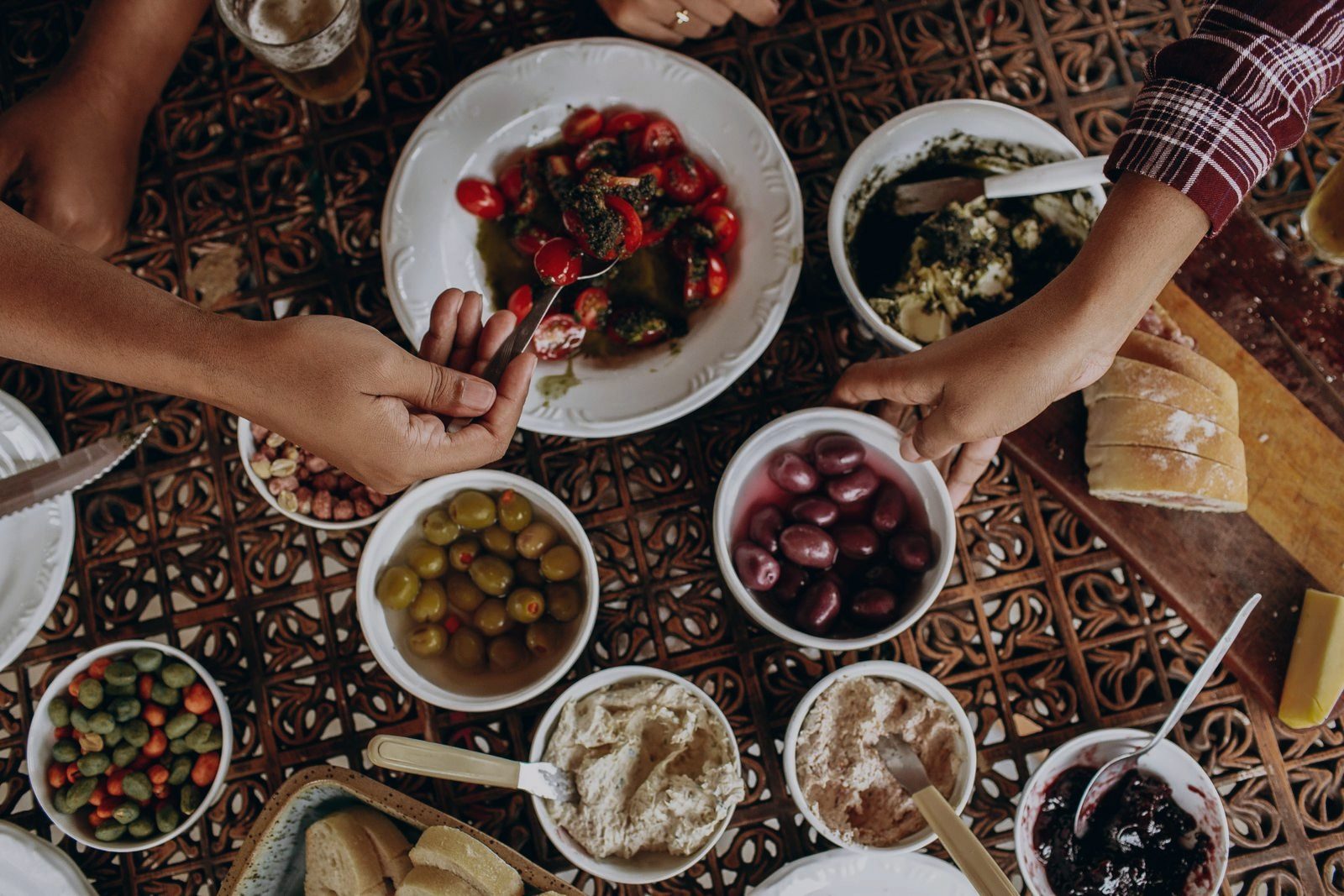 A shared table shot from directly above — plates of salad, olives, dips and sliced bread, with four hands reaching in